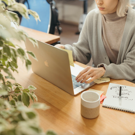 A photo of a woman sitting at an office desk in front of a laptop, her face partially out of frame.