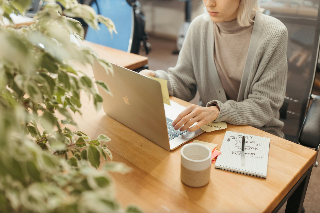 A photo of a woman sitting at an office desk in front of a laptop, her face partially out of frame.